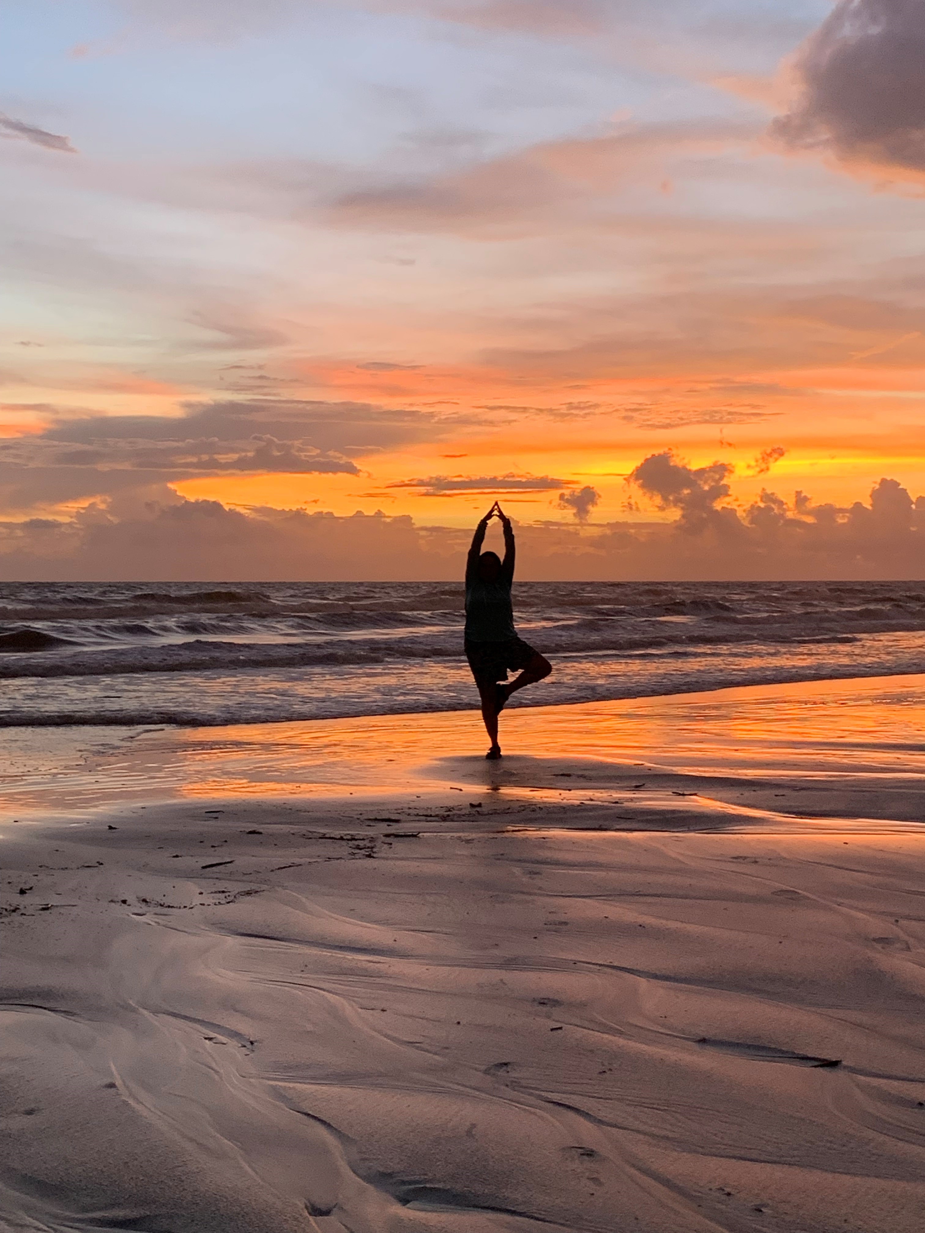 Person on a beach at sunset practicing yoga